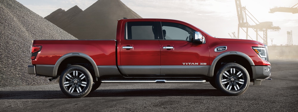 2024 Nissan TITAN in red, profile view with gravel piles in the background