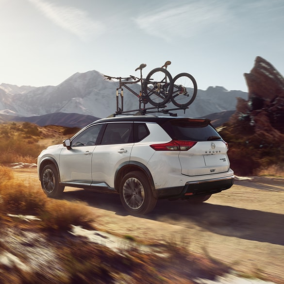 2024 Nissan Rogue driving on a dirt road, with two bicycles attached to the roof rail crossbars