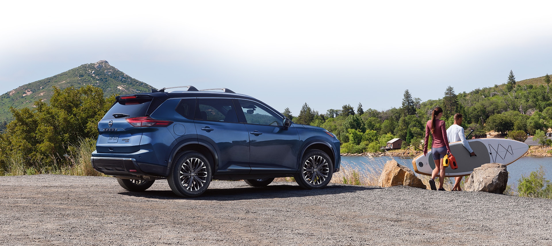 2024 Nissan Rogue parked lakeside, with paddleboarders moving toward the lake