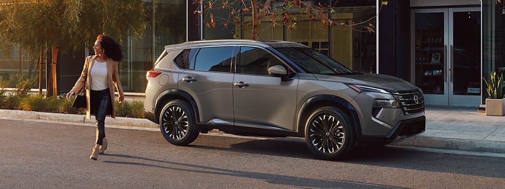 2024 Nissan Rogue side profile parked on a city street, with the driver walking away in the sun