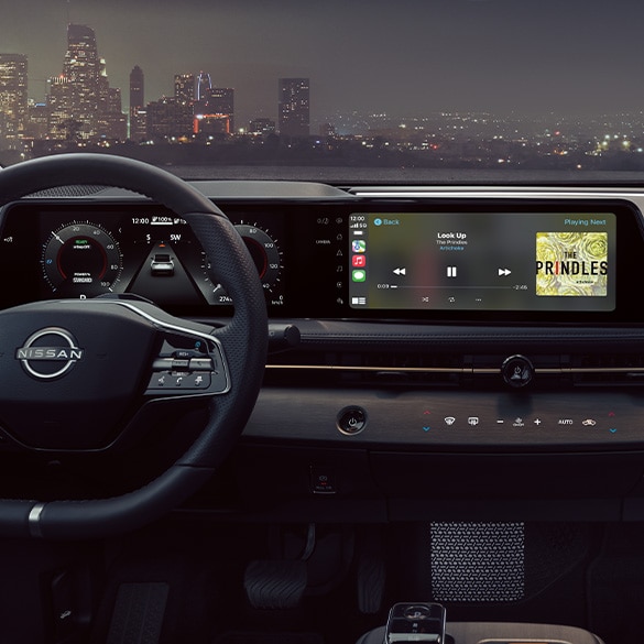 2024 Nissan Ariya showing cockpit touch screen to illustrate advanced tech at night with cityscape in the background 