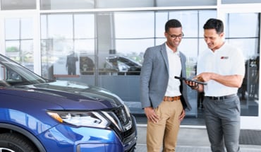 Nissan Salesperson Looking At Tablet With Customer