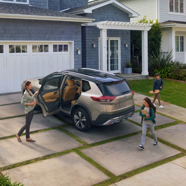 mom opening silver Nissan Rogue door for child in front of a house 