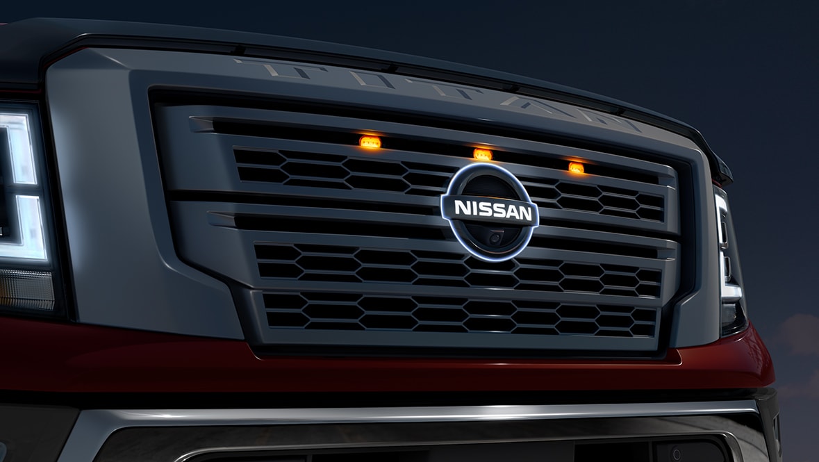 2021 Nissan TITAN front grille in the dark with LED headlights on and center badge illuminated