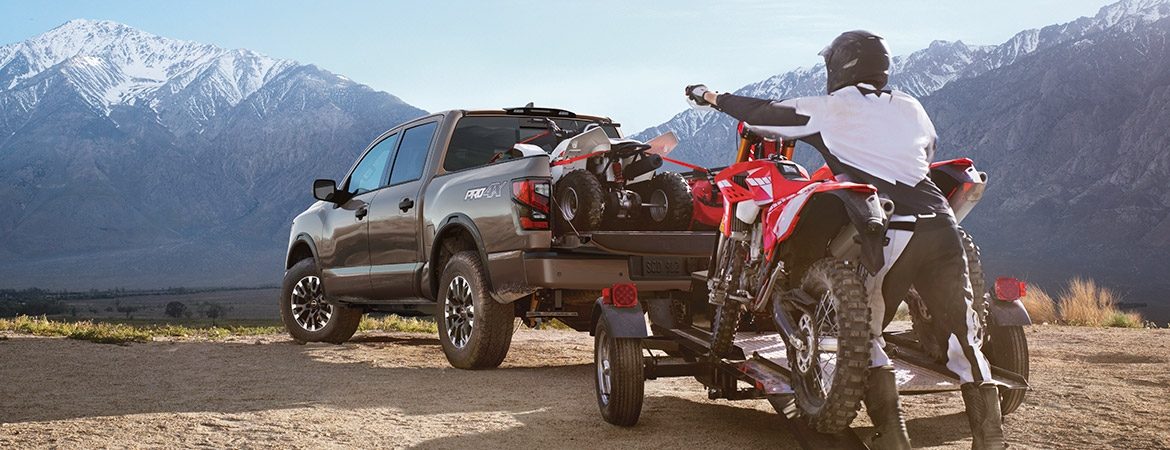 2023 Nissan TITAN person loading motorcycles onto a trailer in the mountains.