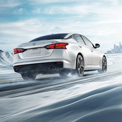 2024 Nissan Altima in white seen from behind driving in snowy landscape illustrating all-wheel drive 