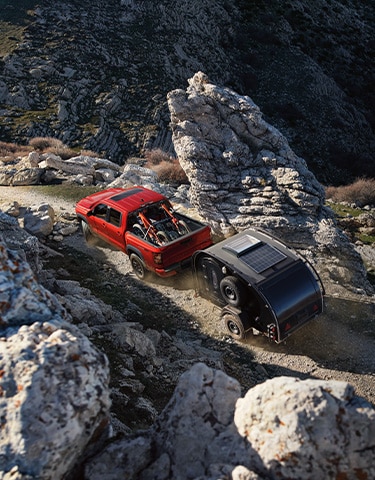 2024 Nissan Frontier, top view, towing a trailer through a rocky landscape, with some motorbikes in the truck bed