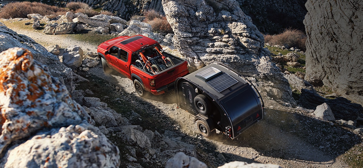 Red Nissan frontier towing a small camper through extreme rocky terrain