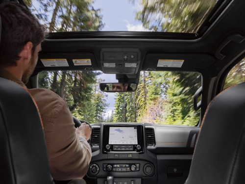 2024 Nissan Frontier interior view showing center screen and a forest view through the windshield and moonroof