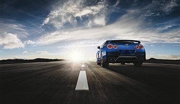 2023 Nissan GT-R in Bayside Blue driving toward the sun on an open road.