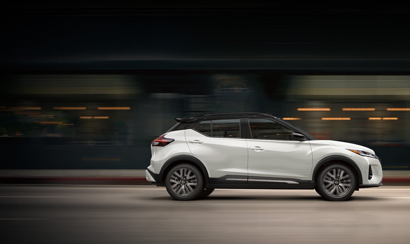 2024 Nissan Kicks in white, profile driving on a downtown street