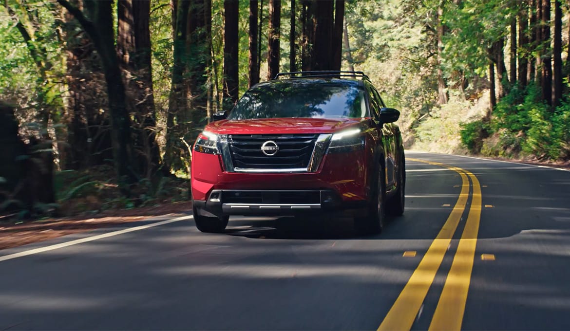 2024 Nissan Pathfinder front view, driving down a tree-lined mountain road.