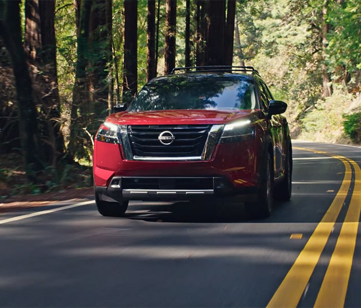 2024 Nissan Pathfinder front view driving down a tree-lined mountain road.