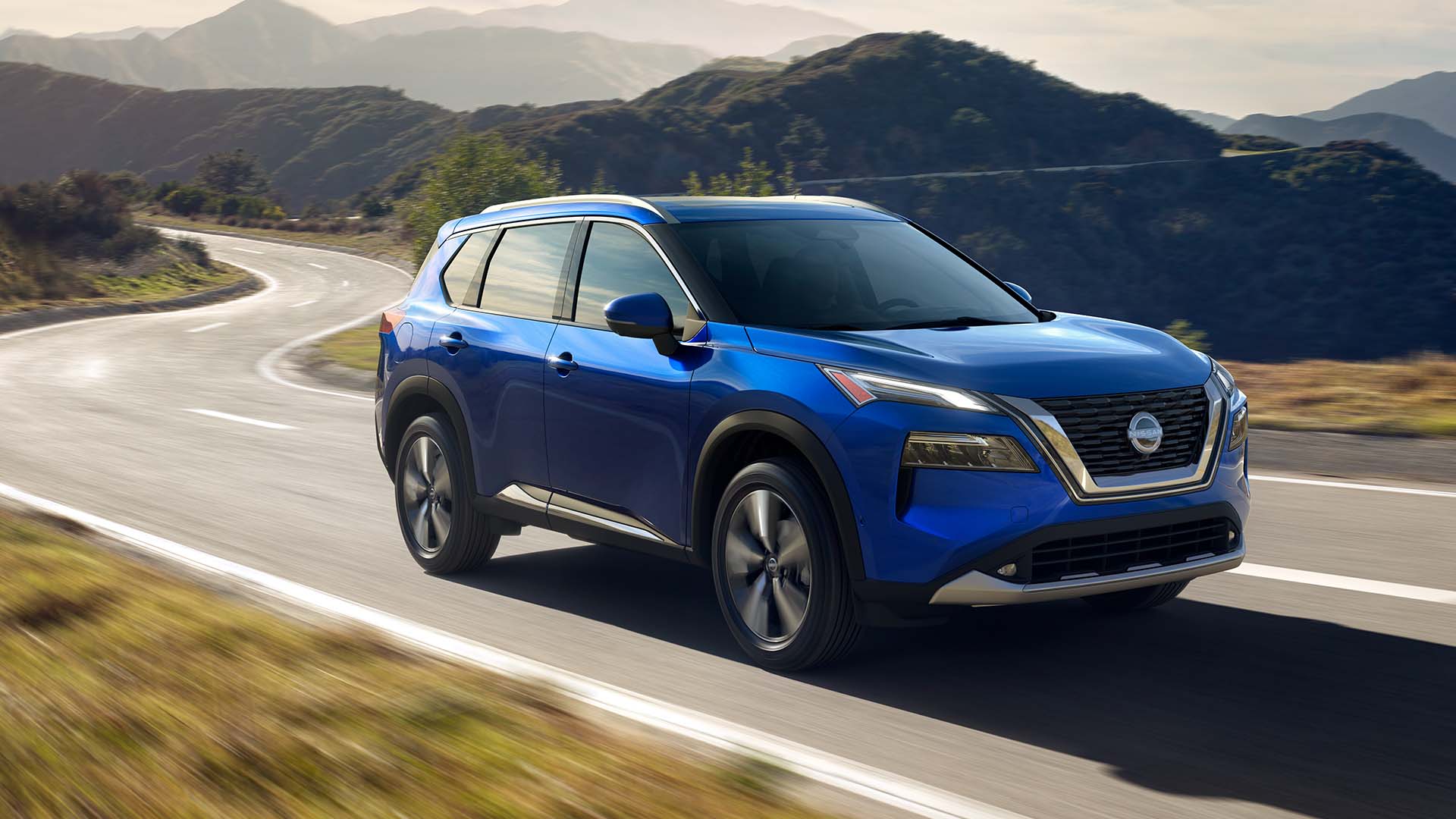 Blue NIssan Rogue driving down a curved road, surrounded by hills and trees