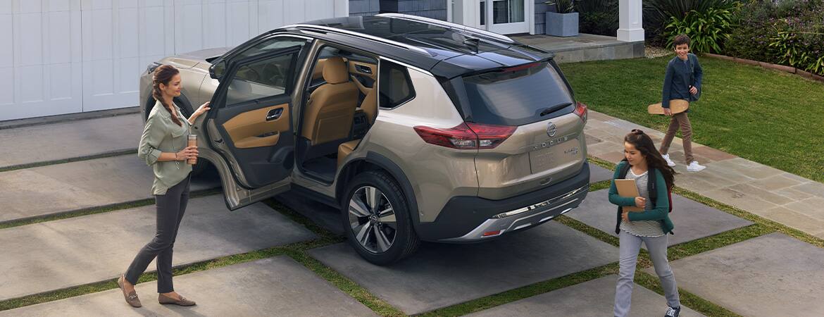 2023 Nissan Rogue in a driveway with door open and family about to get in.