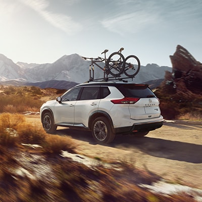 2024 Nissan Rogue driving on a dirt road, with two bicycles attached to the roof rails