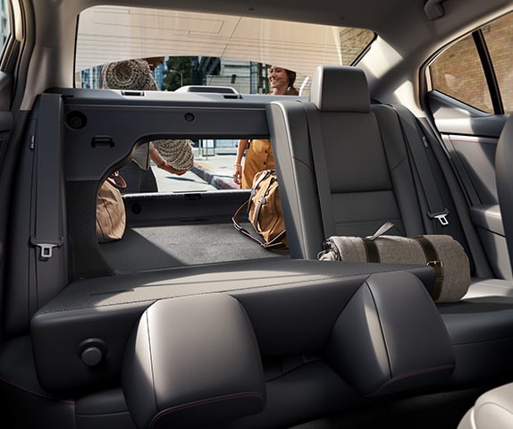 2024 Nissan Sentra displaying people putting a rug into the cargo space with one of the 60/40 split rear seats up and one down.